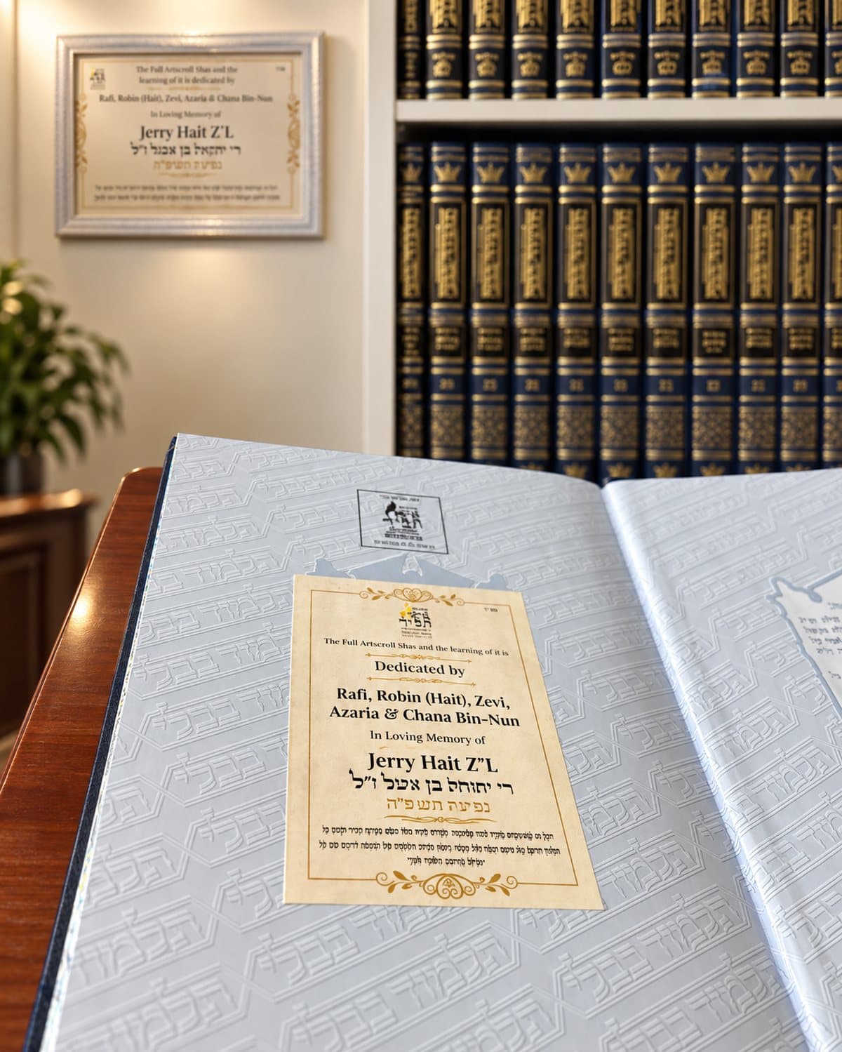 A printed dedication plate inside a sponsored sefer, with a shelf of sefarim behind